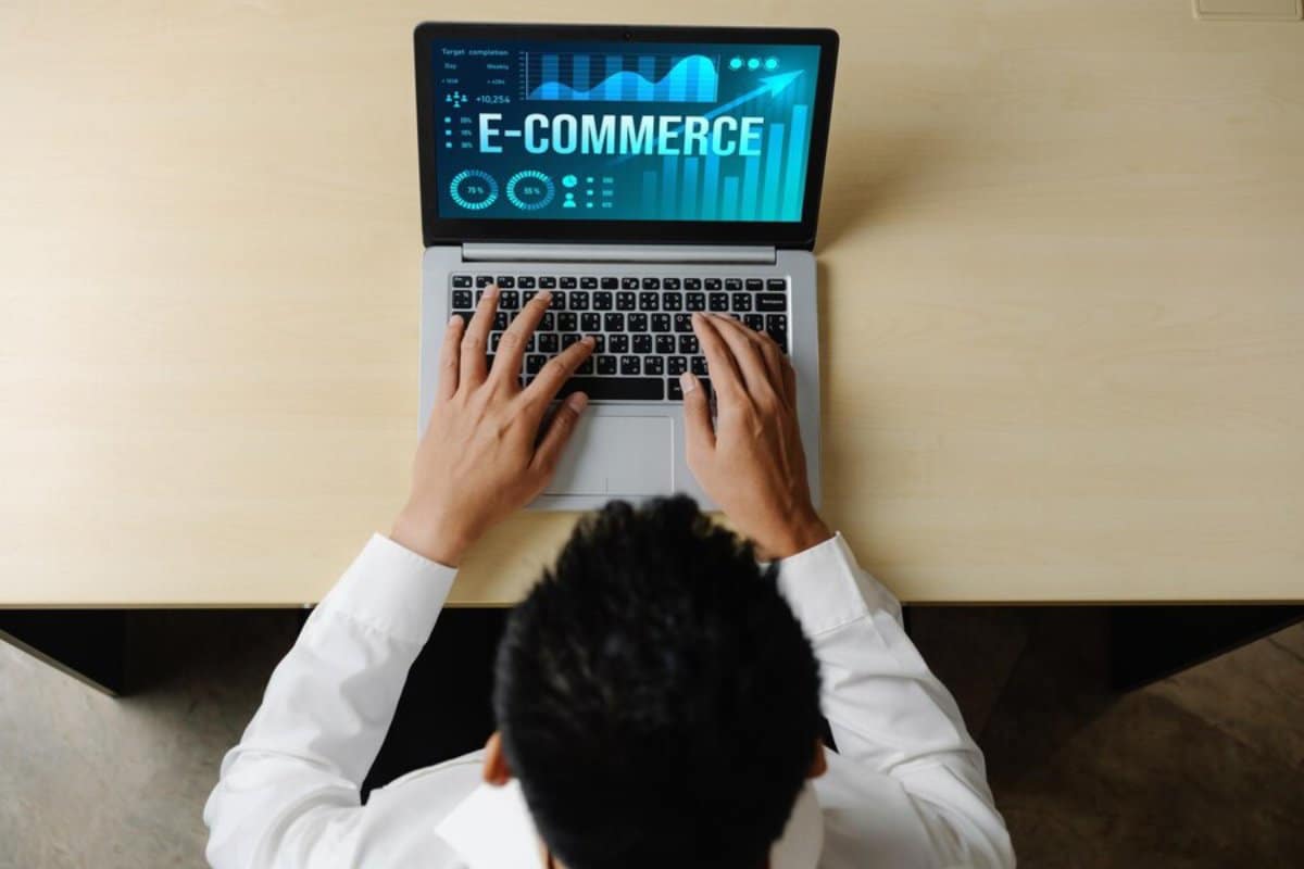 Person in white shirt using a laptop displaying e-commerce graphics on the screen, viewed from above.