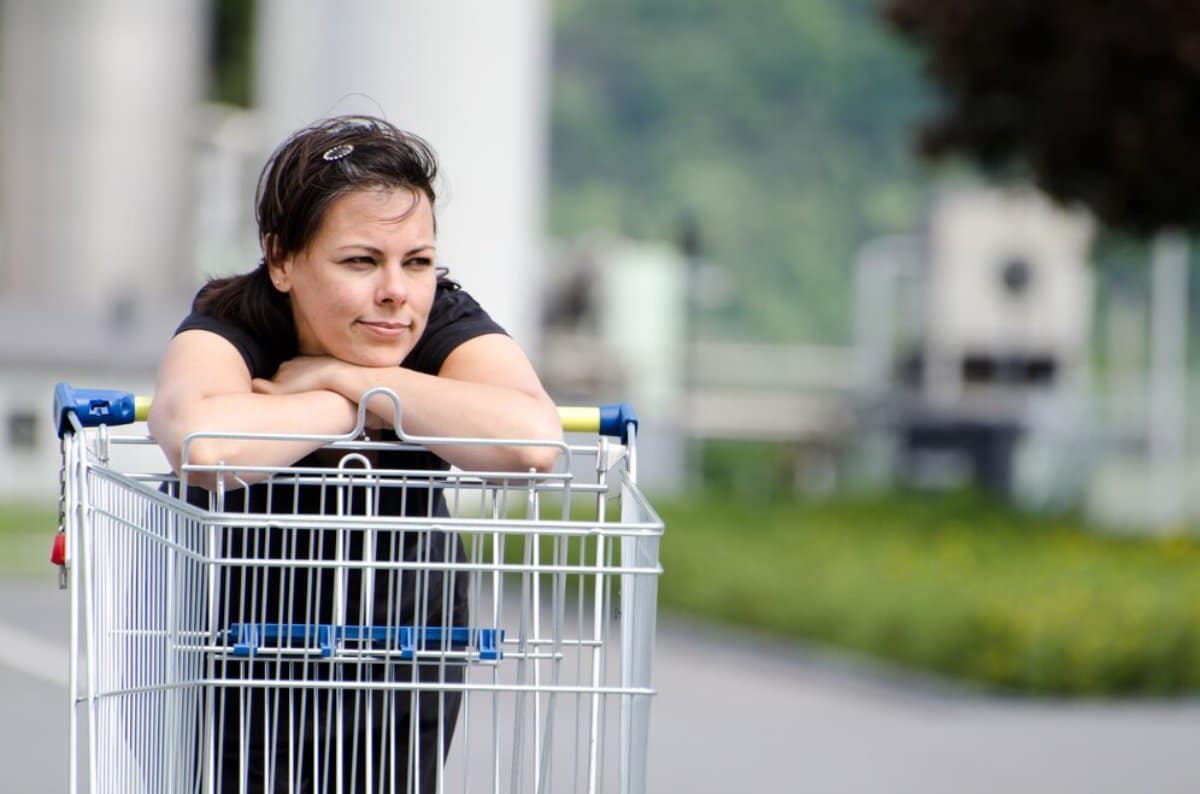 Woman leaning on a shopping cart outdoors, looking thoughtful.