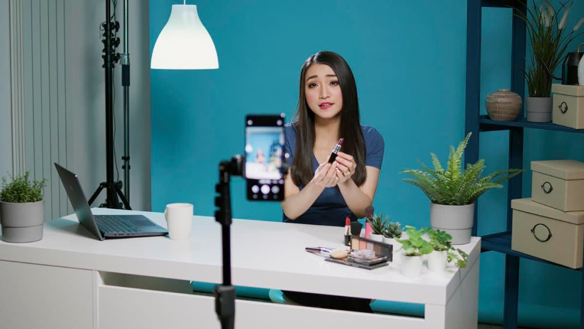 A woman records a makeup tutorial using her smartphone in a well-organized, stylish room.