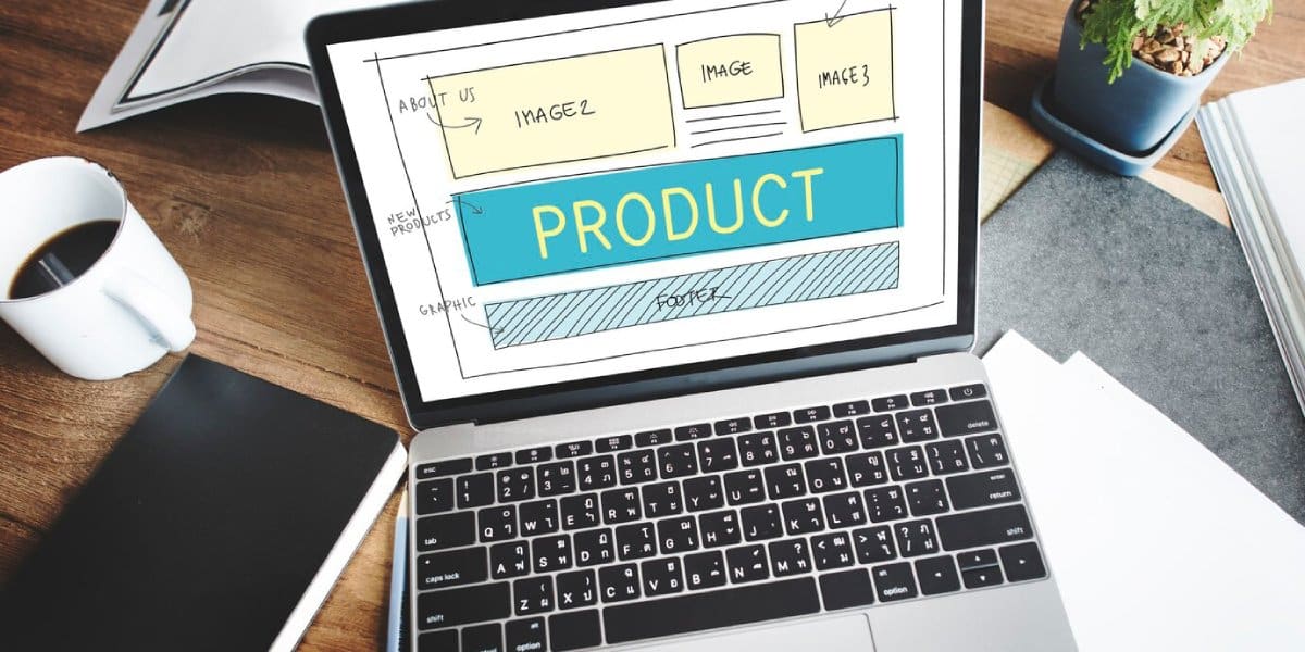Laptop displaying a website design mockup with labeled sections, next to a coffee cup and documents on a wooden desk.