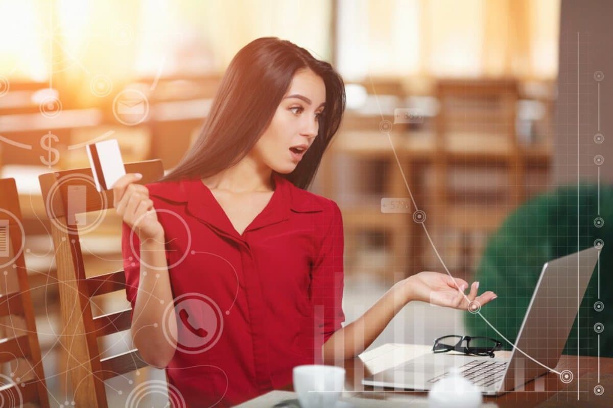 A surprised woman in a red blouse using a laptop, surrounded by floating digital icons and graphics.