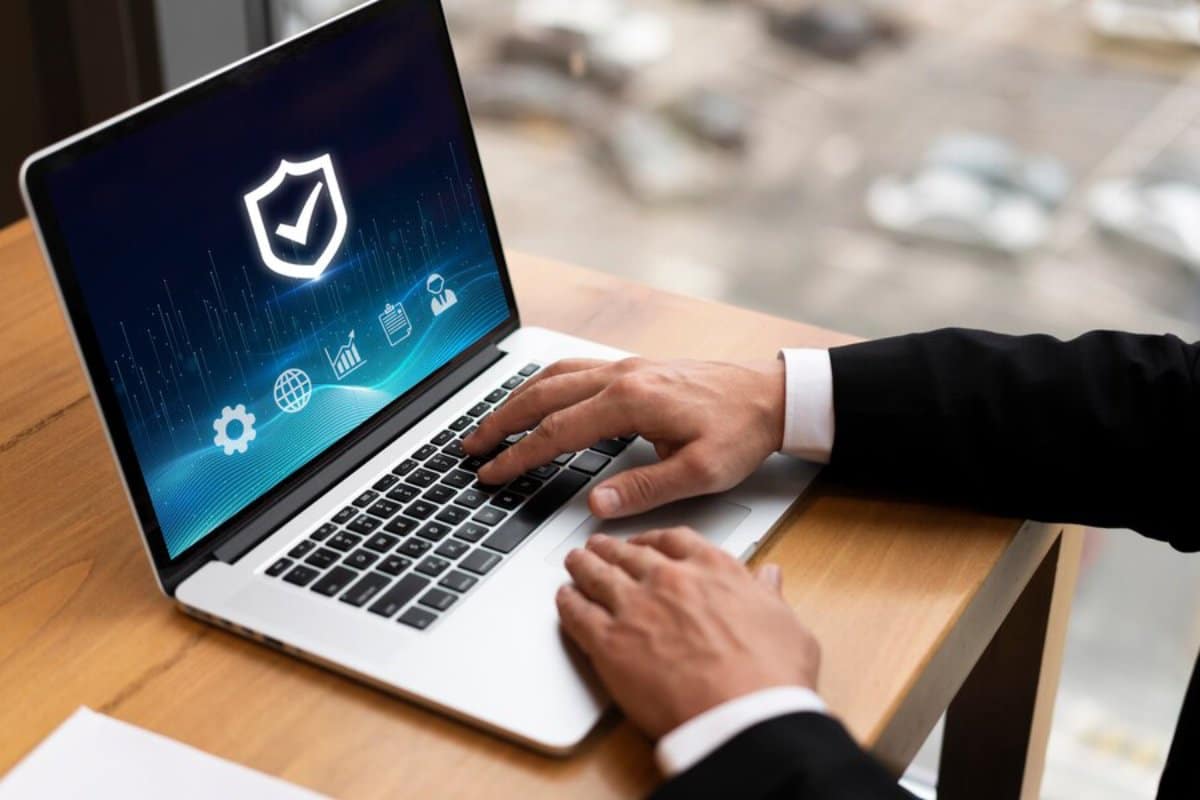 Person using a laptop displaying cybersecurity symbols on the screen, with hands on the keyboard in an office environment.