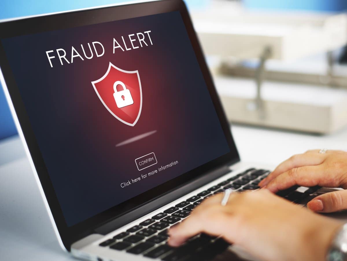 Person using a laptop displaying a "Fraud Alert" message with a security shield icon.
