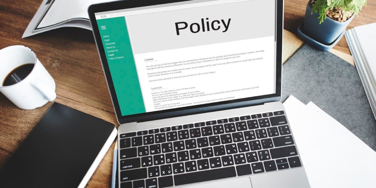 Laptop displaying a "Policy" document on a desk with a coffee cup and notebooks.