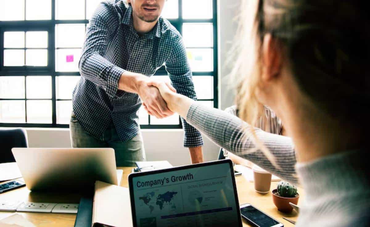 A man and woman shake hands showing partnership , with a laptop displaying "Company's Growth" in the foreground.